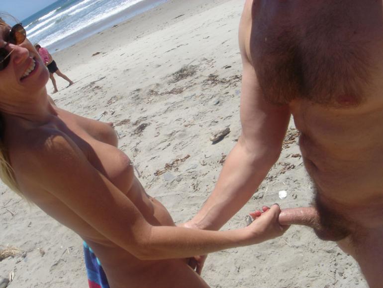 Wife with round breasts stroking cock at nude beach picture